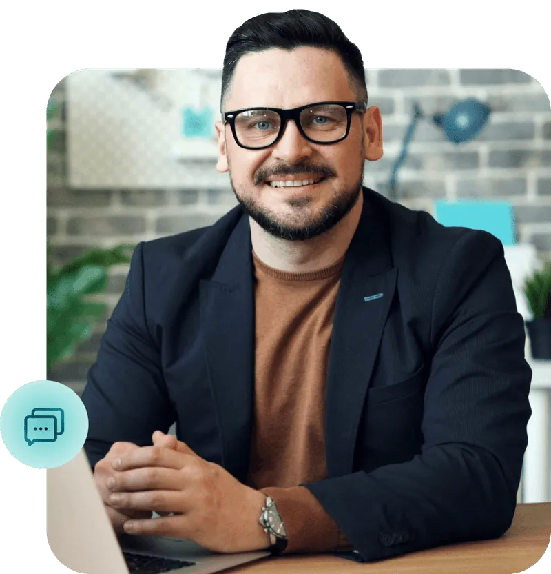 Smiling professional man in glasses and blazer sitting at a desk with a laptop, representing customer support or business communication services